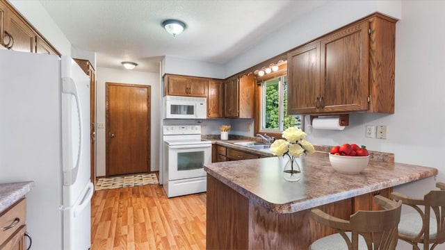 kitchen with a peninsula, a sink, light wood-type flooring, white appliances, and a breakfast bar area