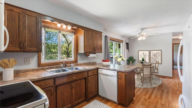 kitchen featuring white appliances, a peninsula, ceiling fan, light wood finished floors, and a sink