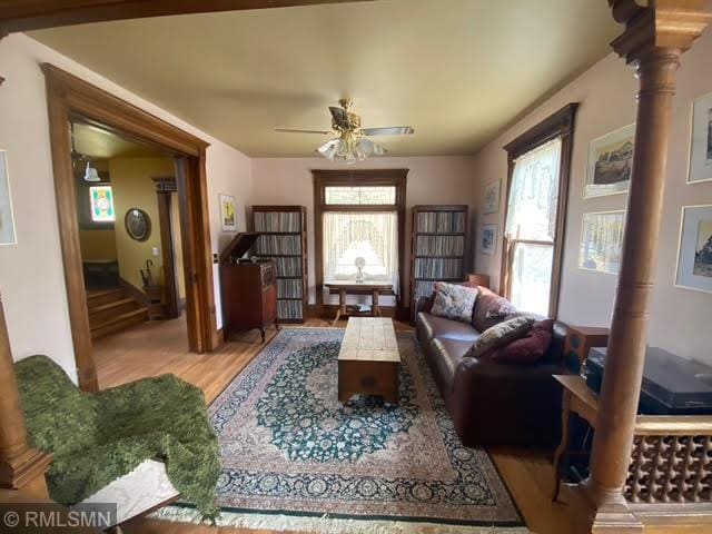 living room featuring ceiling fan, wood finished floors, and decorative columns