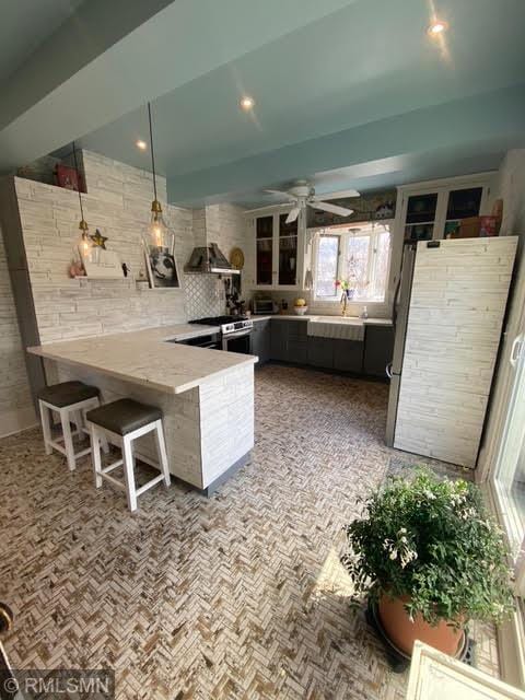 kitchen featuring a breakfast bar, a sink, a peninsula, stainless steel range, and ceiling fan