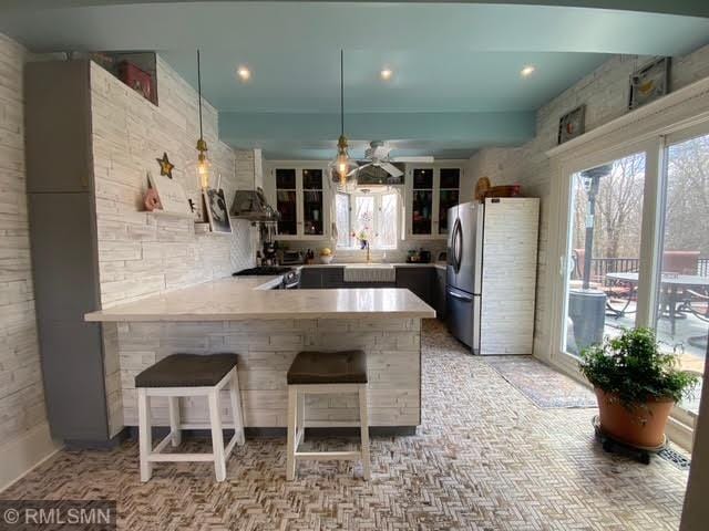 kitchen featuring light countertops, a ceiling fan, freestanding refrigerator, a peninsula, and glass insert cabinets