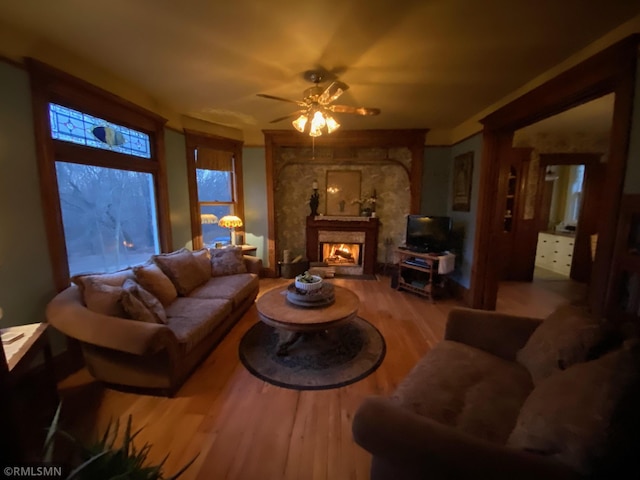 living room with a high end fireplace, wood finished floors, and a ceiling fan