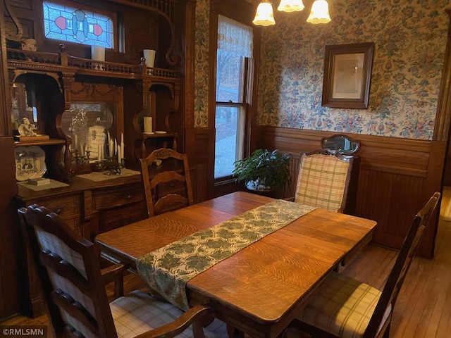 dining area with wood-type flooring, a healthy amount of sunlight, a wainscoted wall, and wallpapered walls
