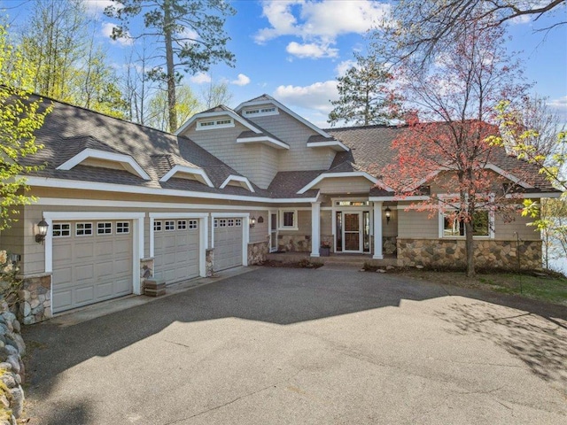 view of front of property with stone siding, driveway, a garage, and roof with shingles
