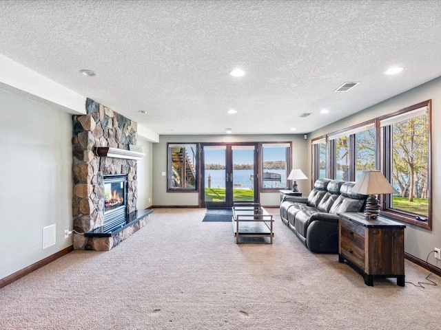 living room featuring light carpet, baseboards, a textured ceiling, a stone fireplace, and a water view