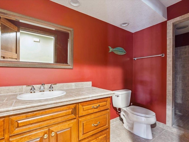 bathroom featuring toilet, tile patterned flooring, vanity, and a tile shower