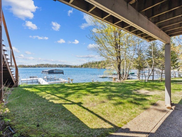 view of grassy yard with a water view and a boat dock