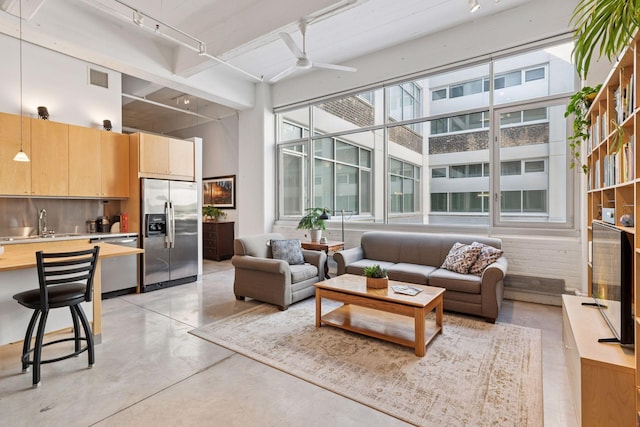 living room featuring rail lighting, concrete floors, ceiling fan, and a high ceiling