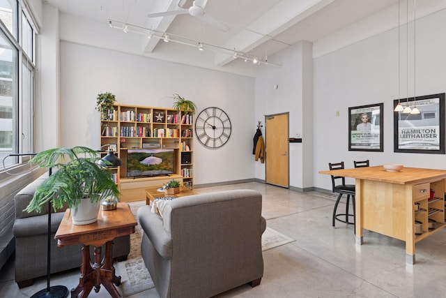 living room with finished concrete flooring, track lighting, ceiling fan, a high ceiling, and baseboards