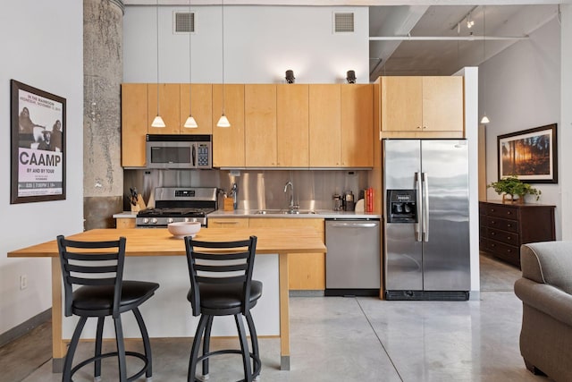 kitchen featuring stainless steel appliances, a sink, concrete flooring, a high ceiling, and a breakfast bar