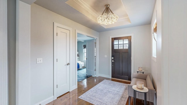 entryway with baseboards, a tray ceiling, wood finished floors, and a notable chandelier