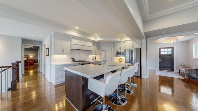 kitchen with dark wood-style flooring, crown molding, a sink, under cabinet range hood, and stainless steel appliances