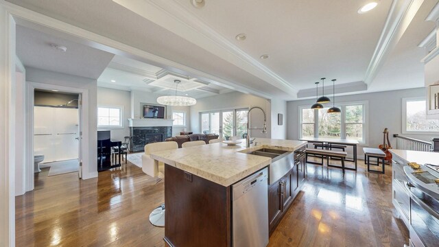 kitchen with a kitchen island with sink, hanging light fixtures, stainless steel dishwasher, a sink, and dark wood-style floors