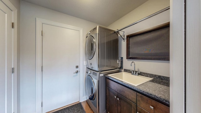 washroom with stacked washer and dryer, a sink, cabinet space, and wood finished floors