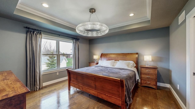 bedroom with recessed lighting, baseboards, wood finished floors, a tray ceiling, and ornamental molding