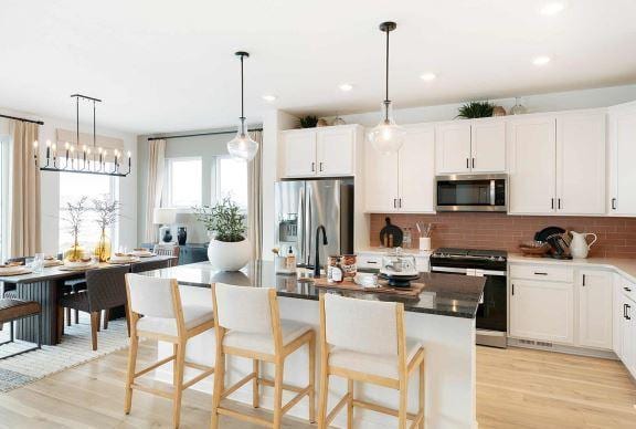 kitchen with stainless steel appliances, a kitchen island with sink, light wood-style floors, and backsplash