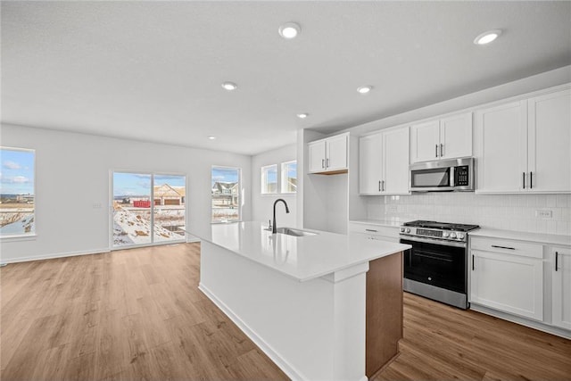 kitchen with stainless steel appliances, light wood-style flooring, a sink, a center island with sink, and backsplash