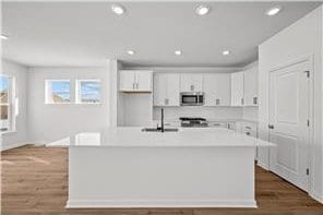 kitchen featuring white cabinets, light countertops, a sink, stainless steel microwave, and dark wood-style flooring