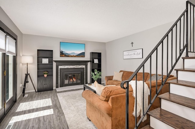 living area featuring a textured ceiling, a glass covered fireplace, baseboards, wood finished floors, and stairs