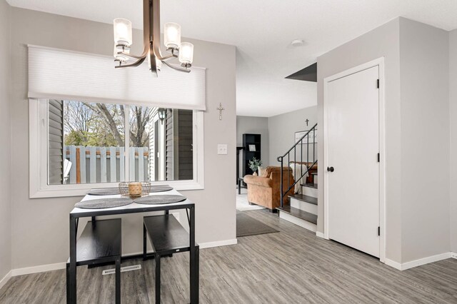 dining space with stairway, baseboards, a chandelier, and wood finished floors