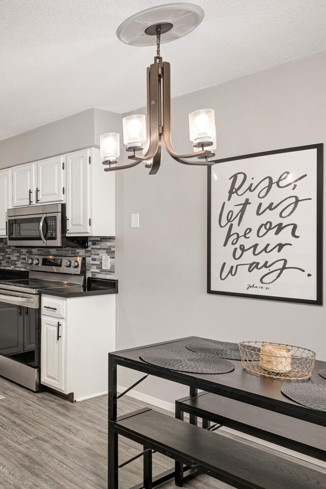 kitchen featuring dark countertops, tasteful backsplash, an inviting chandelier, stainless steel appliances, and white cabinetry