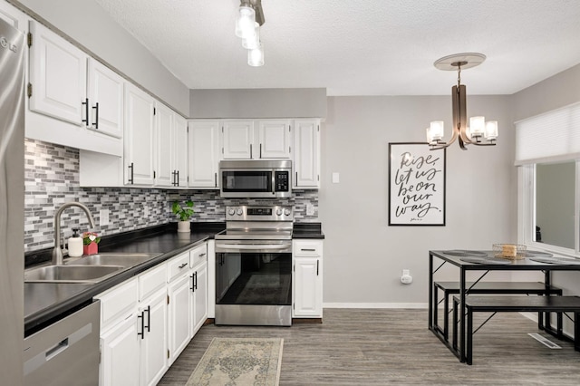 kitchen with a sink, tasteful backsplash, dark countertops, dark wood-type flooring, and appliances with stainless steel finishes