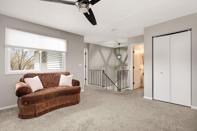 living area with carpet, a ceiling fan, baseboards, and an upstairs landing