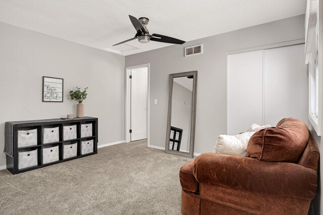 sitting room with a ceiling fan, a textured ceiling, carpet floors, baseboards, and visible vents