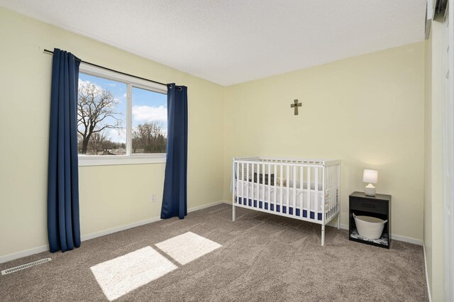 carpeted bedroom featuring visible vents, a crib, and baseboards