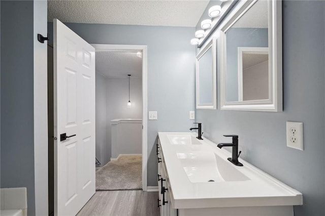 full bath with double vanity, a textured ceiling, wood finished floors, and a sink