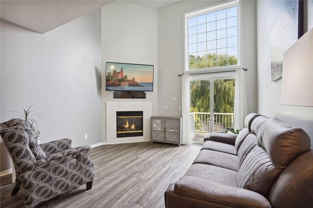 living room with a tiled fireplace, wood finished floors, a towering ceiling, and plenty of natural light