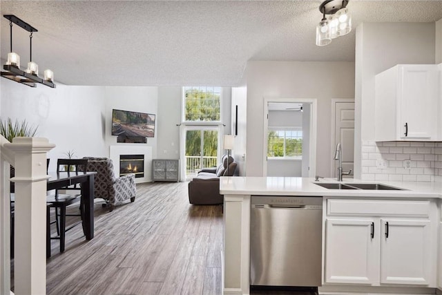 kitchen featuring a sink, a glass covered fireplace, a textured ceiling, dishwasher, and open floor plan