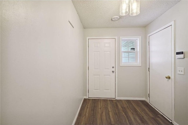 doorway featuring a notable chandelier, a textured ceiling, dark wood-style flooring, and baseboards