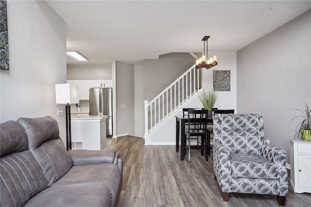 living room featuring visible vents, dark wood-style floors, baseboards, a notable chandelier, and stairs
