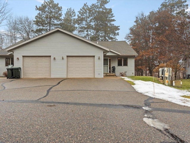 ranch-style house featuring an attached garage, a shingled roof, and aphalt driveway