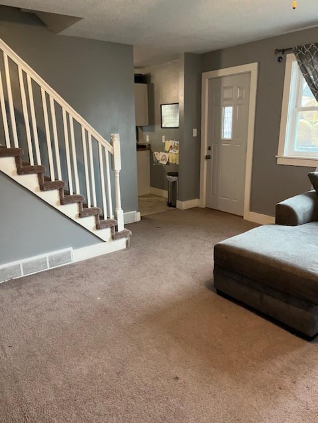 living room with a textured ceiling, visible vents, carpet floors, baseboards, and stairs