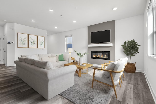 living area with recessed lighting, a glass covered fireplace, wood finished floors, and baseboards