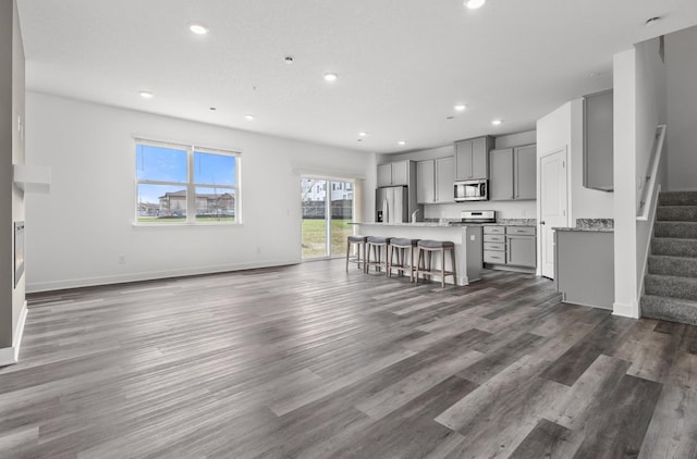 unfurnished living room featuring recessed lighting, dark wood-type flooring, and stairs