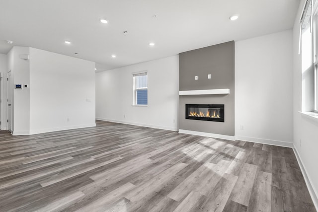 unfurnished living room with baseboards, wood finished floors, a glass covered fireplace, and recessed lighting