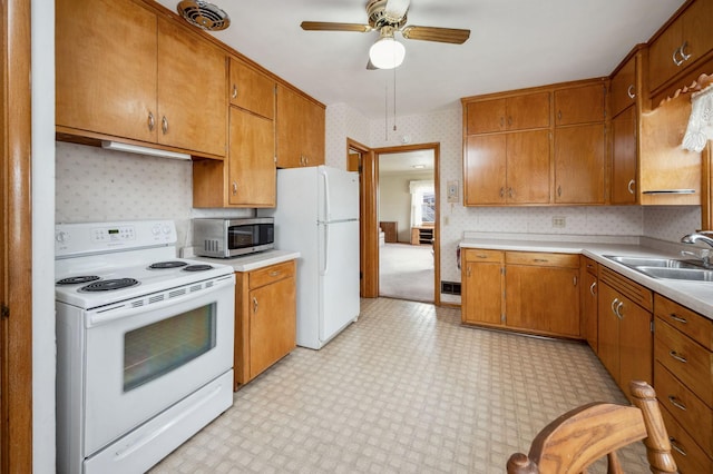 kitchen featuring ceiling fan, a sink, white appliances, light countertops, and wallpapered walls