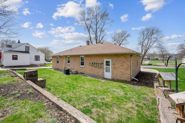 rear view of property featuring brick siding, a shingled roof, a lawn, and a chimney