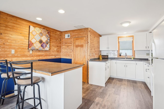 kitchen featuring a breakfast bar area, visible vents, a sink, wooden walls, and white cabinetry