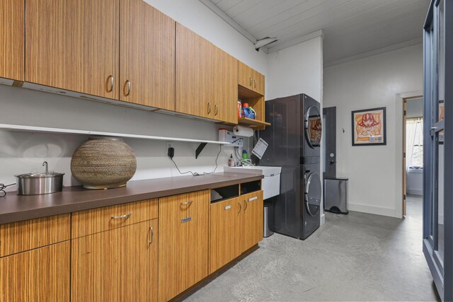 laundry area with a sink, baseboards, stacked washer and dryer, and cabinet space