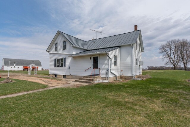 rear view of house featuring a chimney, a standing seam roof, a lawn, and metal roof