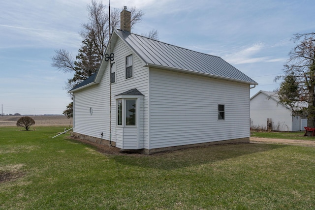 view of home's exterior with a lawn, a chimney, a standing seam roof, and metal roof