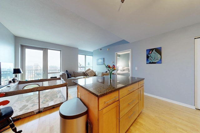 kitchen with light wood-type flooring, dark stone counters, open floor plan, baseboards, and a kitchen island