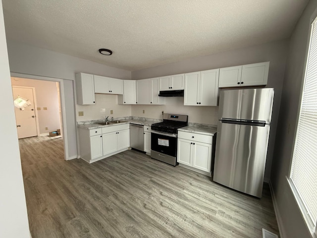 kitchen featuring under cabinet range hood, stainless steel appliances, light countertops, a sink, and a textured ceiling