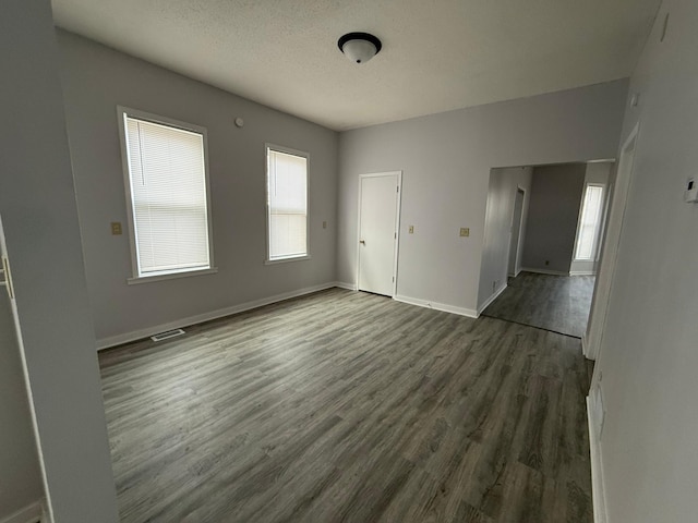 spare room with baseboards, visible vents, a textured ceiling, and dark wood-style flooring