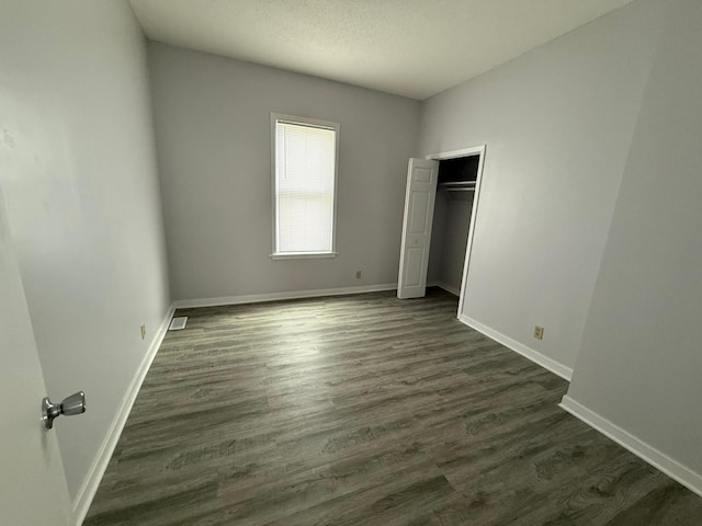 unfurnished bedroom with baseboards, dark wood-type flooring, visible vents, and a closet