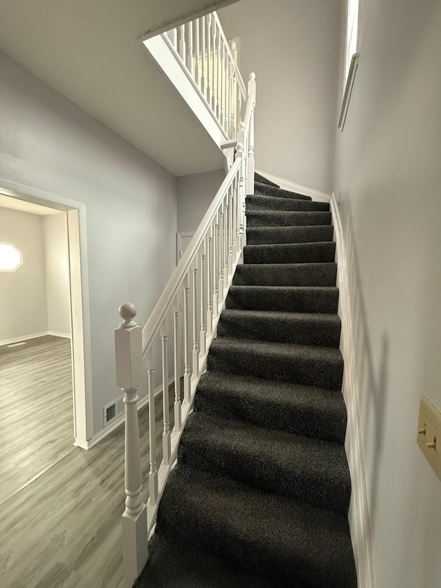 staircase with baseboards, wood finished floors, and visible vents